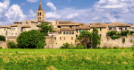Una scena di un borgo storico con case in pietra e un campanile che si staglia contro un cielo azzurro.