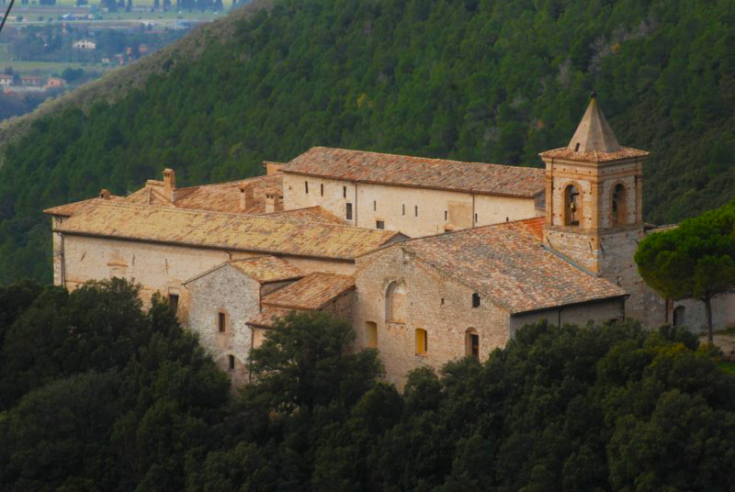 Un antico eremo immerso in un ambiente naturale, circondato da alberi e colline, che richiama l'eredità spirituale e culturale.