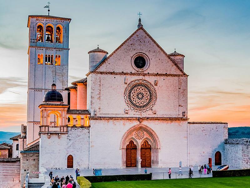 La Basilica di San Francesco d'Assisi al tramonto, circondata da un'armonia di colori e luci.