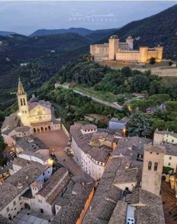 Panorama di un antico borgo con un palazzo e una chiesa, circondato dalla natura umbra.