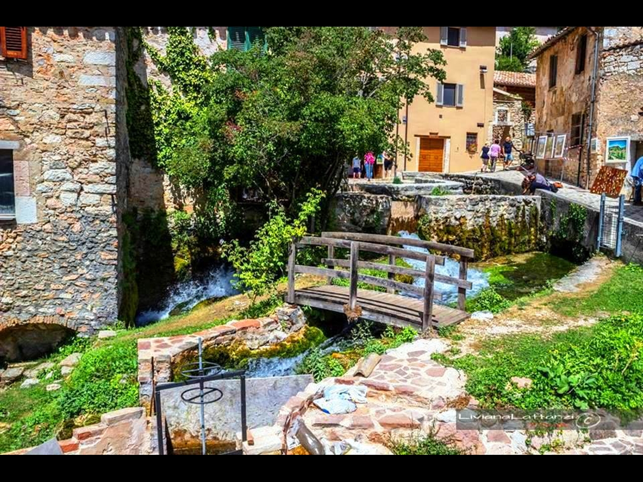 Un tranquillo paesaggio di villaggio con case in pietra, un ponte in legno e un piccolo ruscello.
