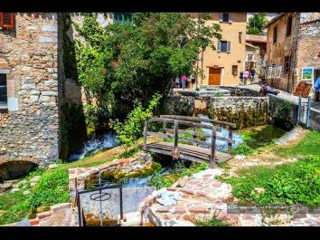 Un tranquillo paesaggio di villaggio con case in pietra, un ponte in legno e un piccolo ruscello.