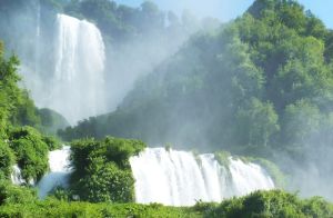 Una cascata immersa nella vegetazione, con spruzzi d'acqua che brillano alla luce.
