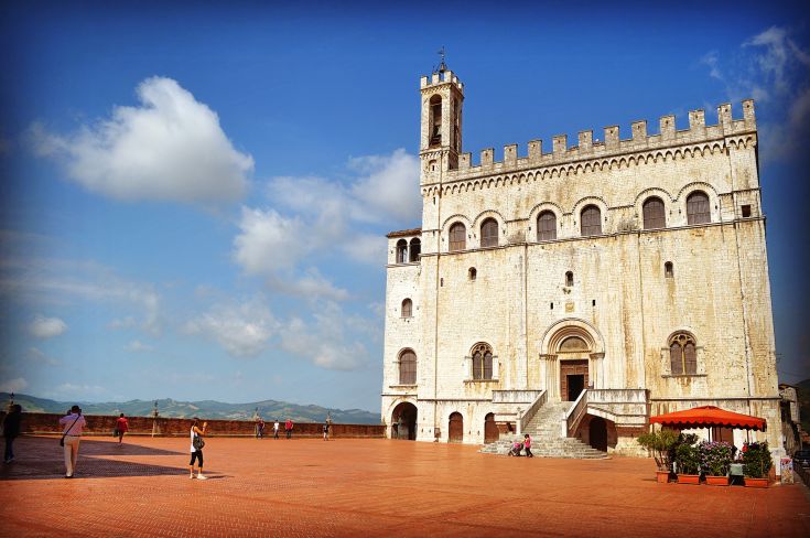 Scena di un palazzo storico situato in una piazza, circondato da persone e sotto un cielo sereno.