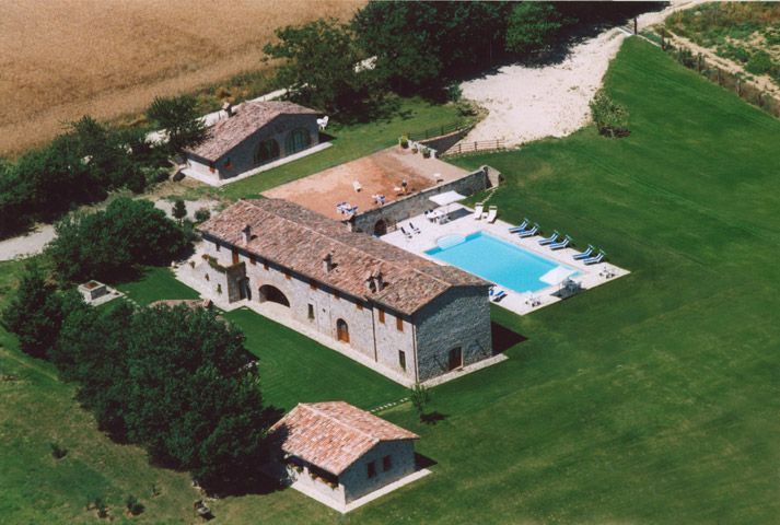 Scena aerea di una villa con piscina, circondata da un ampio verde e alberi.