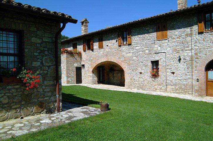 Una fattoria in pietra immersa nella campagna, circondata da prati verdi e fiori colorati.