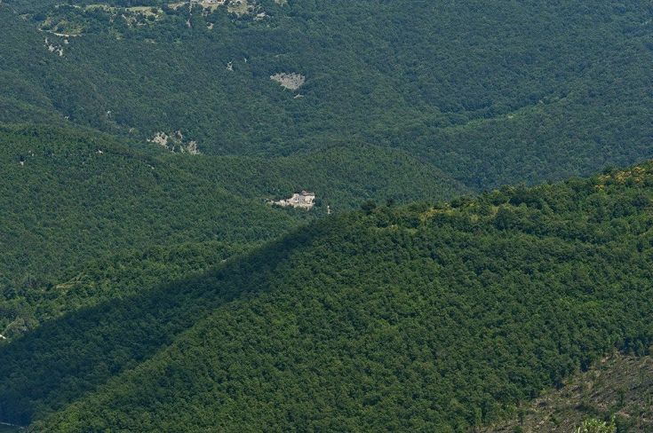 Un panorama di colline verdi e alberi, con un villaggio visibile in lontananza.