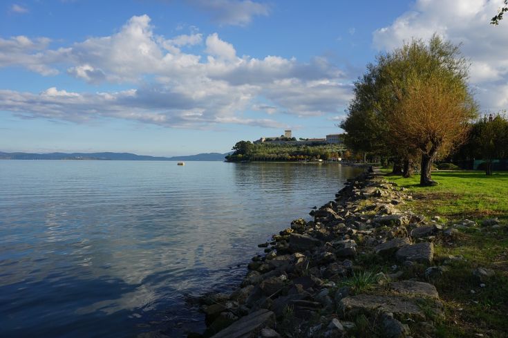 Una scena tranquilla sul lago, circondato da alberi verdi e nuvole che si riflettono nell'acqua.