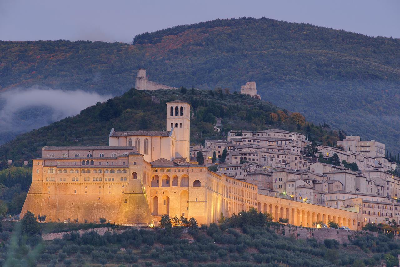 Scena della Basilica di San Francesco ad Assisi, illuminata di sera nel contesto tranquillo della città.