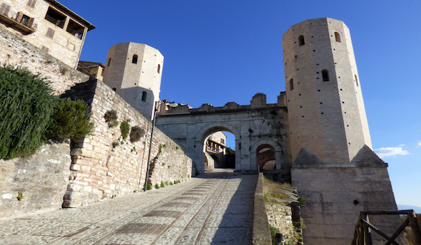 La porta d'ingresso con torri storiche e una strada in pietra, illuminata dalla luce del sole.