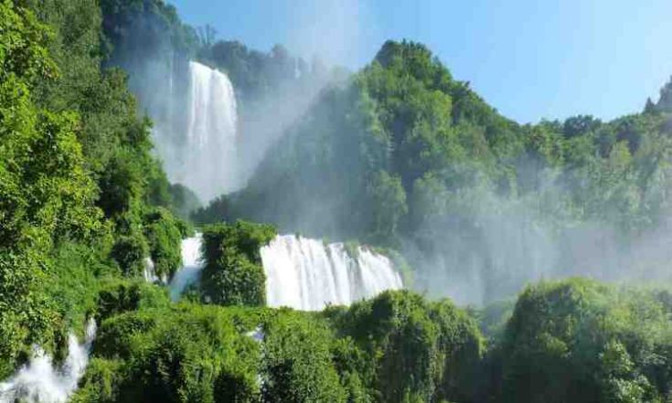 Cascata immersa nella natura, circondata da vegetazione verde e rigogliosa.
