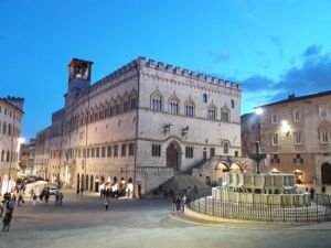 Scena notturna del Palazzo dei Priori e della fontana maggiore illuminata a Perugia.