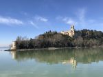 Un castello si riflette nel lago Trasimeno, circondato da alberi e vegetazione.