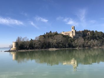 Un castello si riflette nel lago sereno, circondato da alberi e vegetazione.