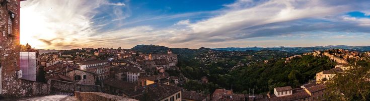 Scena di un borgo umbro, circondato dalla natura, con un cielo sereno e colline verdi.