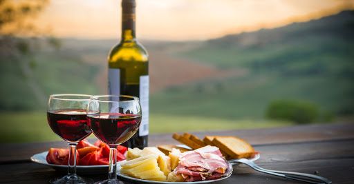 Un momento di condivisione semplice con vino rosso, salumi e formaggi su un tavolo all'aperto.