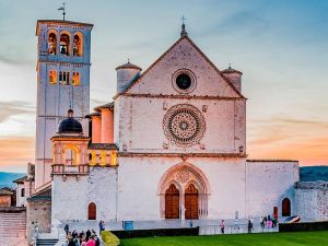 La Basilica di San Francesco, situata ad Assisi, si presenta imponente al tramonto, immersa in un'atmosfera suggestiva.