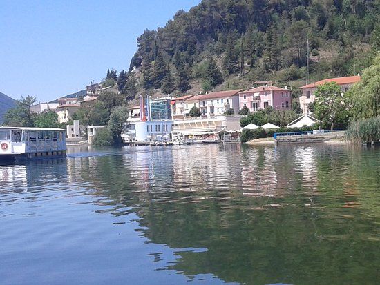 Un tranquillo panorama sul lago, con i riflessi dei palazzi nell'acqua e la natura sullo sfondo.