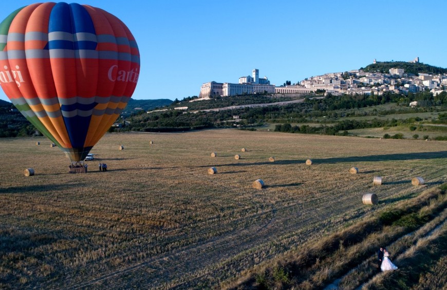 Una mongolfiera si libra sopra i campi umbri, offrendo una vista suggestiva della città di Assisi.
