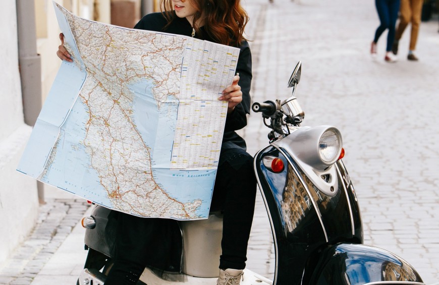 Una ragazza consulta una mappa mentre è seduta su uno scooter parcheggiato.