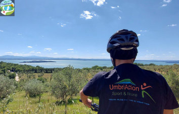 in bici lungo il lago Trasimeno - Un ciclista osserva il Lago Trasimeno da un punto panoramico, circondato da vegetazione e cielo sereno.