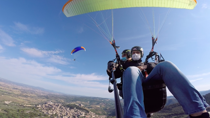 Due persone praticano il parapendio con uno splendido panorama su un paesaggio collinare.