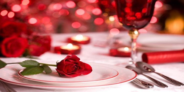 Un tavolo ben apparecchiato con rose rosse, bicchieri e candele per creare un'atmosfera intima durante una cena.