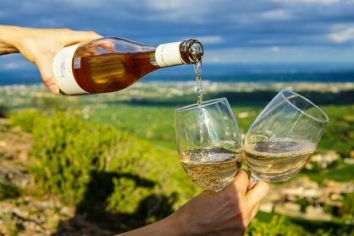 Due bicchieri di vino bianco si uniscono in un tranquillo paesaggio al tramonto.