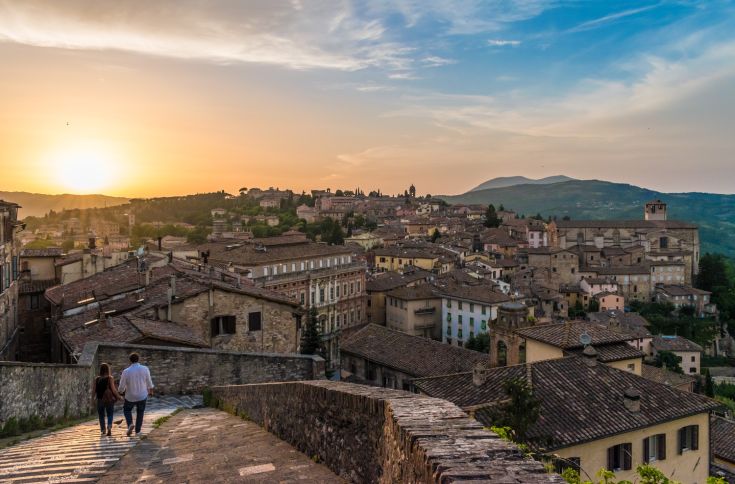 Una coppia passeggia tra le strade di un borgo, illuminate dai colori del tramonto.