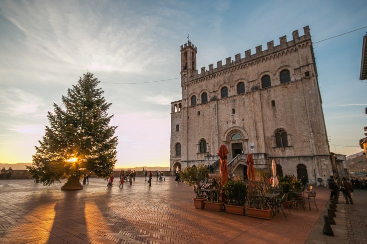 Un tramonto luminoso rischiara la piazza con un albero di Natale e un palazzo di epoca.