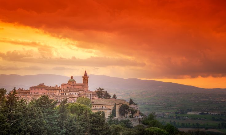 Panorama di un borgo storico, illuminato da un tramonto che colora il cielo di arancione e rosso.