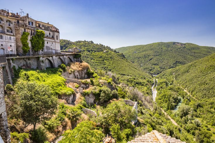 Scena di un tranquillo borgo collinare con edifici antichi e colline verdi circostanti.