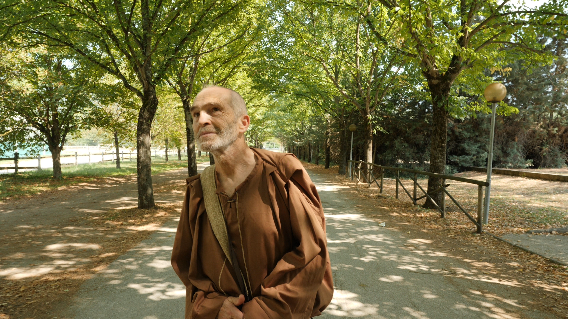 Un uomo in abbigliamento monastico passeggia in un parco verde, circondato da alberi e sentieri tranquilli.