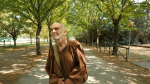 Un uomo in abbigliamento monastico passeggia in un parco verde, circondato da alberi e sentieri tranquilli.
