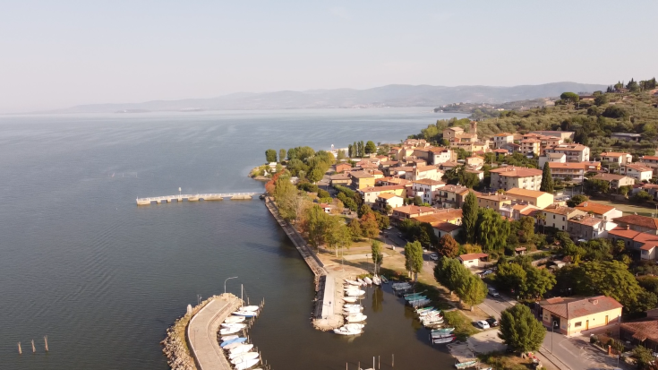 Scena del borgo di Passignano affacciato su un lago, con barche ormeggiate e case dai colori vivaci.