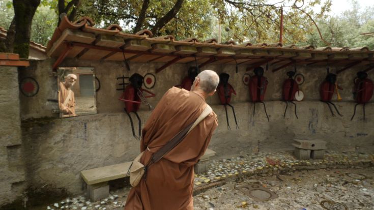 Un uomo osserva il suo riflesso in uno specchio mentre si trova davanti a figure artistiche in un ambiente tranquillo.