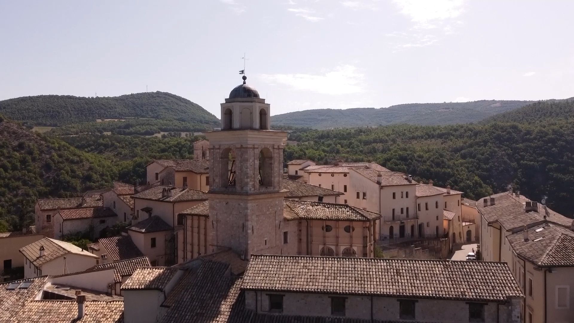 Uno scorcio di un borgo storico con edifici in mattoni e un campanile che si innalza sopra un paesaggio collinare.