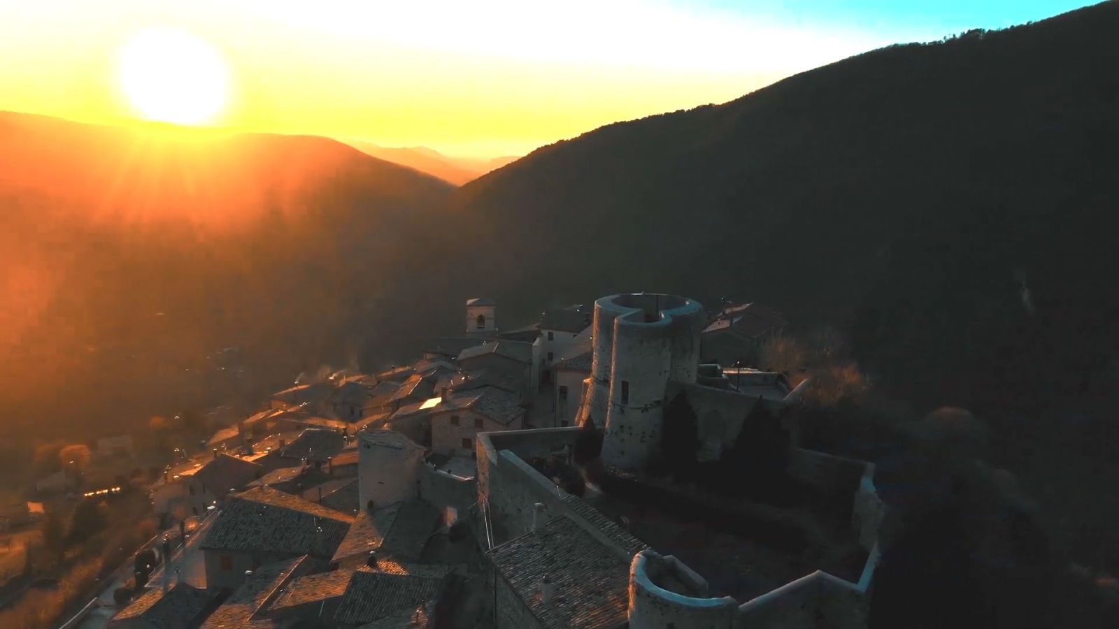 Un tramonto si riflette dolcemente su un borgo storico, circondato da colline verdi, creando un'atmosfera di serenità.