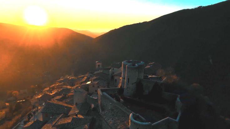 Un tramonto si riflette dolcemente su un borgo storico, circondato da colline verdi, creando un'atmosfera di serenità.