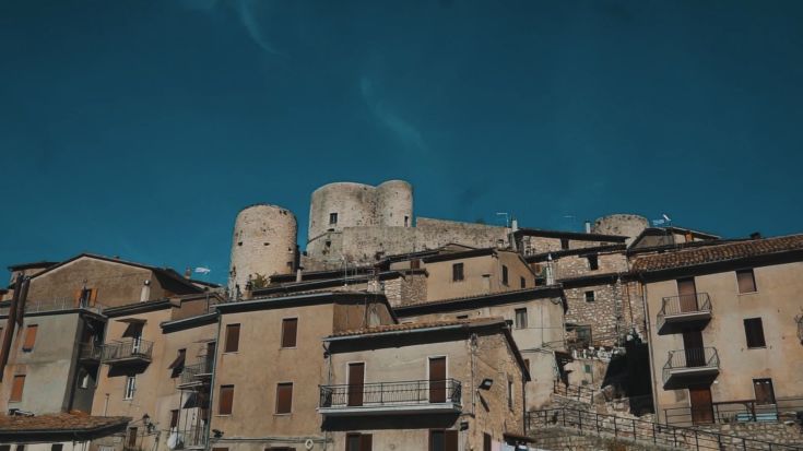 Un borgo con case in pietra e torri storiche sotto un cielo azzurro. Rappresentazione della storia e dell'architettura.
