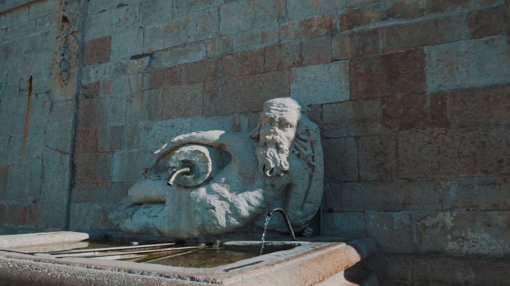 Una fontana storica, in pietra, decorata con una scultura che rappresenta un volto maschile.