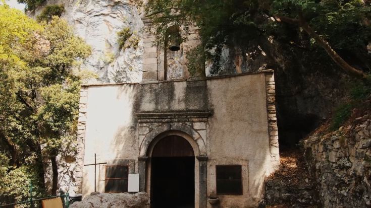 Una chiesa situata tra le rocce, circondata da vegetazione verdeggianti, che crea un'atmosfera tranquilla.