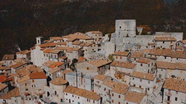 Un panorama di un borgo storico con case in pietra, tetti in tegole e spazi verdi circostanti.
