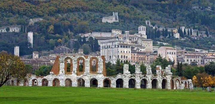 Teatro romano e Antiquarium di Gubbio immerso in un paesaggio verdeggiante, con alberi e vegetazione circostante.