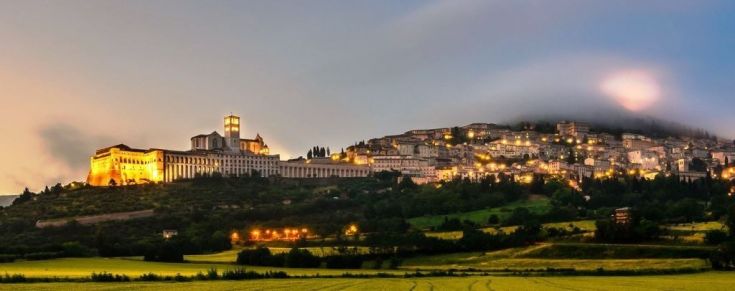 Panorama notturno di Assisi, con illuminazione del palazzo e del paesaggio circostante.