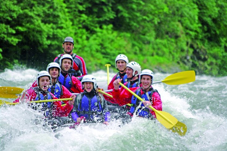 Un gruppo di persone sorridenti mentre partecipano a un'avventura di rafting su un fiume.