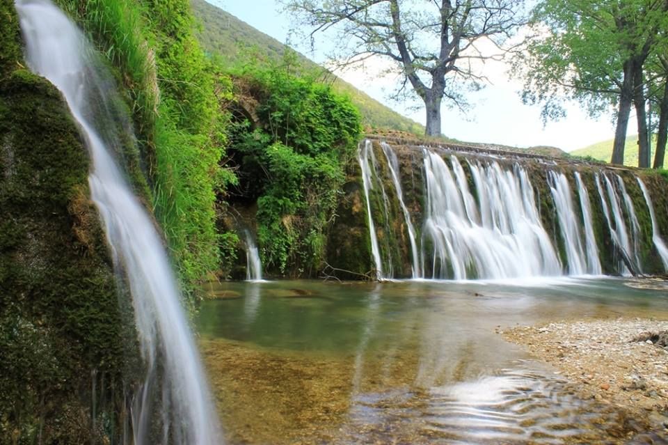 Una scena di cascate immerse nella natura, circondate da alberi verdi e vegetazione. Il suono dell'acqua che scorre crea un'atmosfera tranquilla.