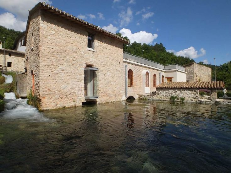 Palazzo in pietra circondato da un lago limpido, inserito in un ambiente naturale.