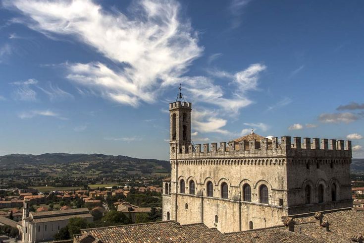 Un castello si erge sopra un paesaggio collinare verde, sotto un cielo azzurro con poche nuvole.