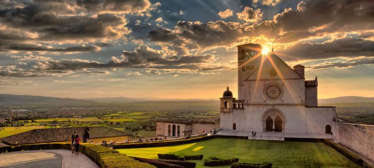 Panorama al tramonto sulla Basilica di San Francesco, circondata dal verde paesaggio umbro.